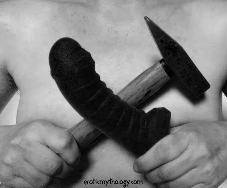 A black-and-white photo of a person holding a hammer and a black dildo in front of their naked chest.