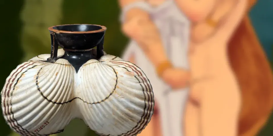 An oil flask decorated with sea shells in the foreground and blurred out bodies in the background.